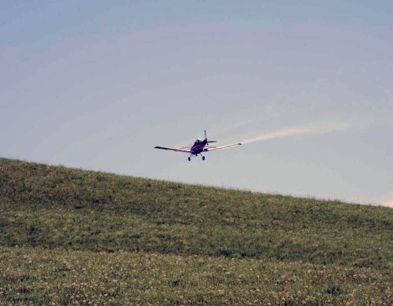 A small aircraft flies close to the ground as it sprays insecticides on rangeland
