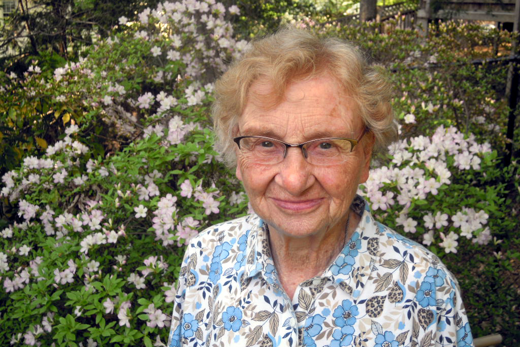 A smiling woman in front of a blooming bush