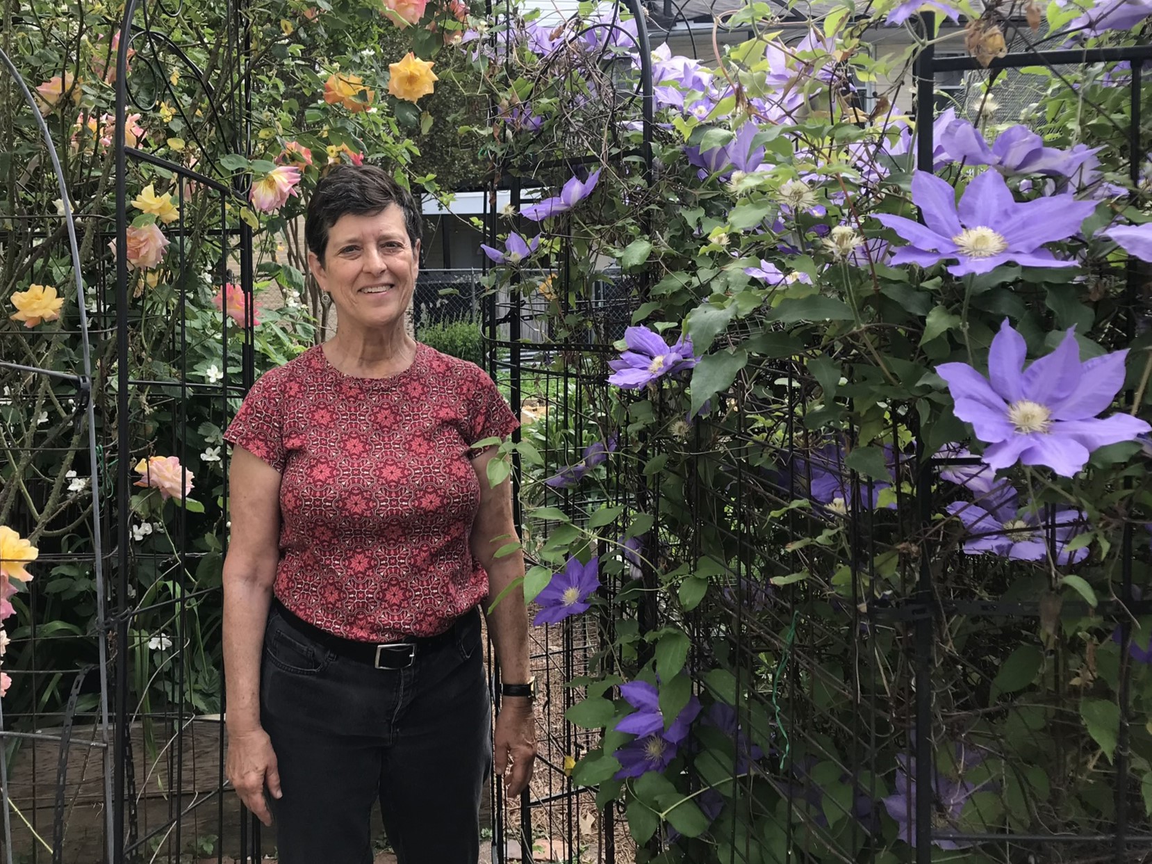 Woman standing next to flowers that are growing up a trellis