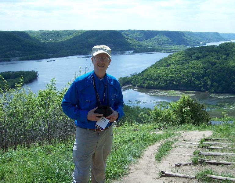 Don Leaon holding a camera in front of a river landscape