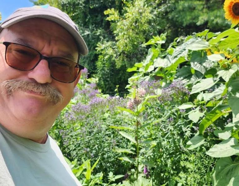 Michael McIntyre smiling in front of tall flowering plants like sunflowers