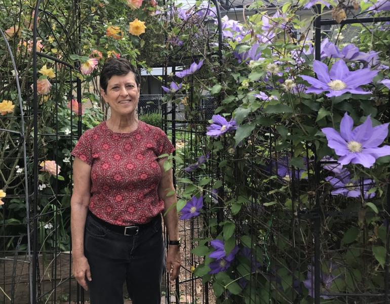 Jan Mooney stands beside purple clematis and yellow rose vines at Upper Fells Point Community Garden