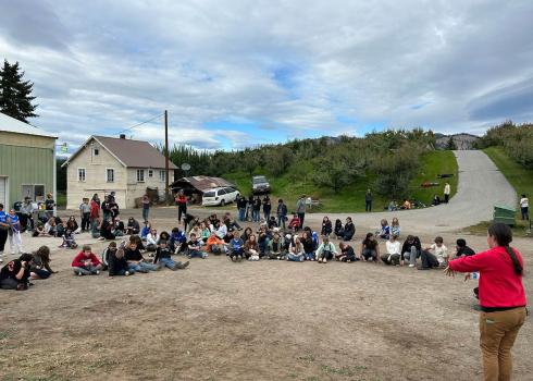 Over a hundred students circle around a speaker, listening to instructions for the day