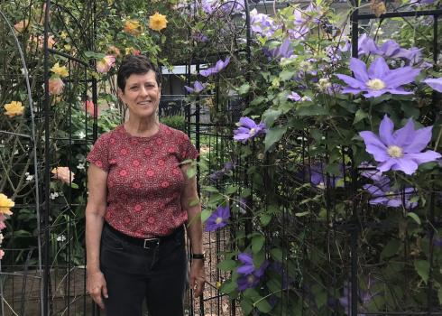 Jan Mooney stands beside purple clematis and yellow rose vines at Upper Fells Point Community Garden