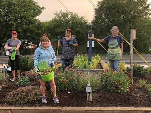 Several Bee City USA participants pose around a flowering garden patch holding garden tools