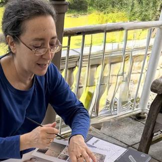 Donna Miskend sits at a table speaking while gesturing to some papers on a table