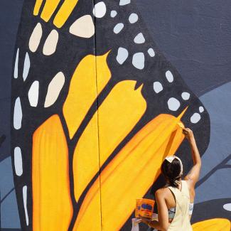 Artist Jane Kim of Ink Dwell studio paints the wing of a giant monarch butterfly, part of the Midnight Dream mural in downtown Orlando, Florida.